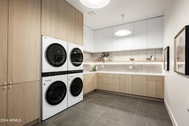 laundry room featuring cabinets, stacked washer and clothes dryer, washing machine and clothes dryer, and dark tile patterned floors