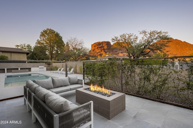 patio terrace at dusk with a fenced in pool, a mountain view, and an outdoor living space with a fire pit