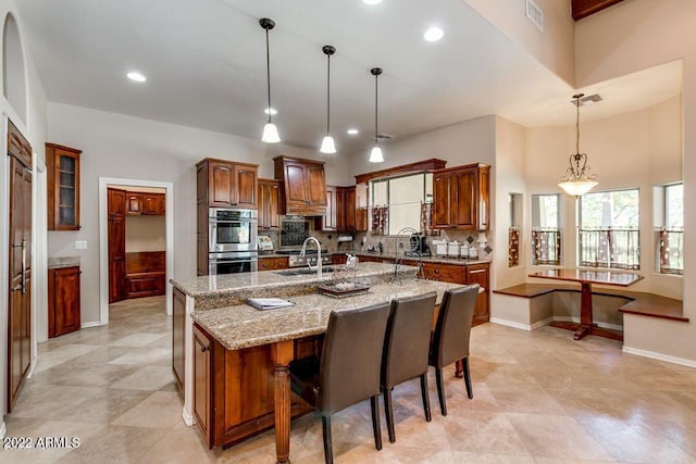 kitchen with backsplash, double oven, a spacious island, sink, and hanging light fixtures