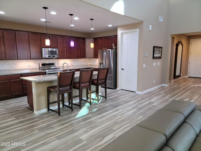 kitchen with a kitchen bar, appliances with stainless steel finishes, backsplash, and pendant lighting