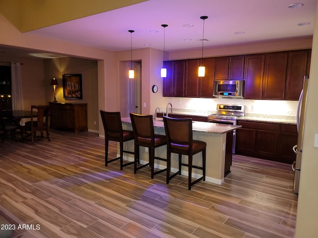 kitchen featuring decorative light fixtures, appliances with stainless steel finishes, wood-type flooring, light stone counters, and a breakfast bar