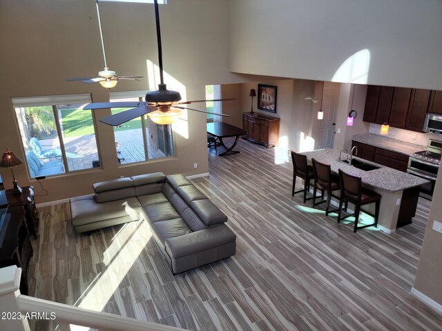 living room with wood-type flooring, sink, ceiling fan, and a high ceiling