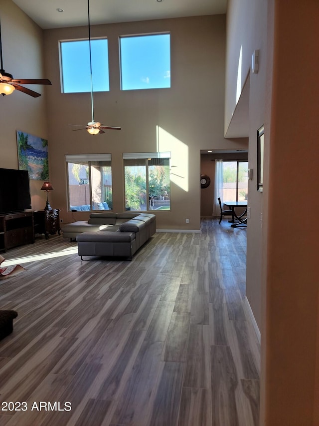 unfurnished living room with ceiling fan, a towering ceiling, and hardwood / wood-style flooring