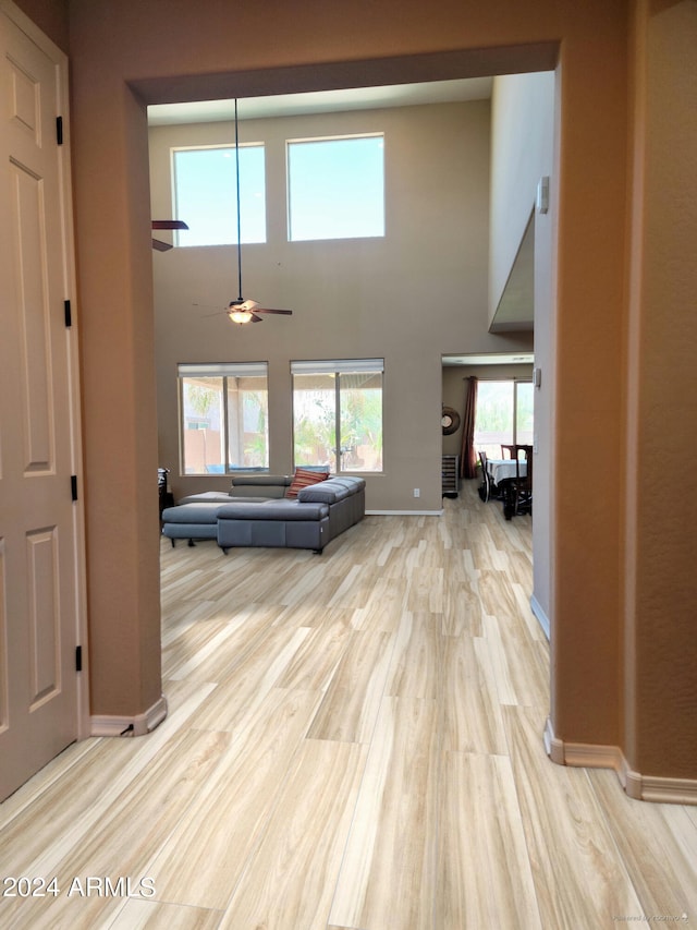 unfurnished living room with ceiling fan, light wood-type flooring, and a towering ceiling