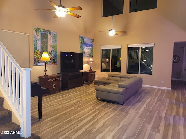 living room with hardwood / wood-style flooring, ceiling fan, and a towering ceiling