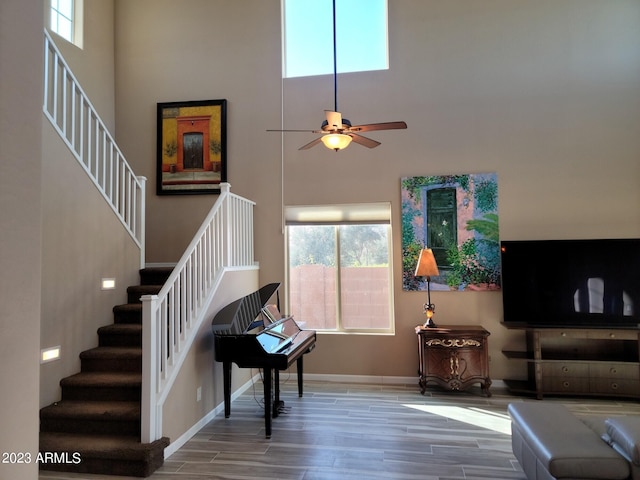 living room featuring ceiling fan, a towering ceiling, and hardwood / wood-style flooring