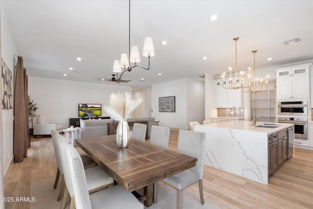 dining room featuring sink, ceiling fan with notable chandelier, and light wood-type flooring