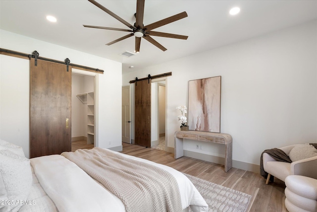 bedroom with a closet, a barn door, ceiling fan, a walk in closet, and light hardwood / wood-style flooring