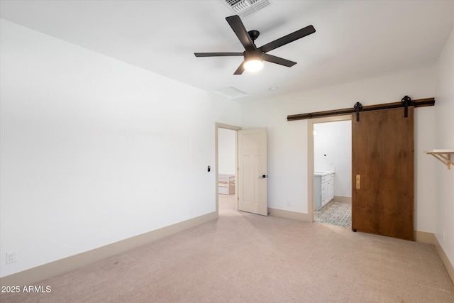 unfurnished bedroom with ensuite bath, ceiling fan, and a barn door