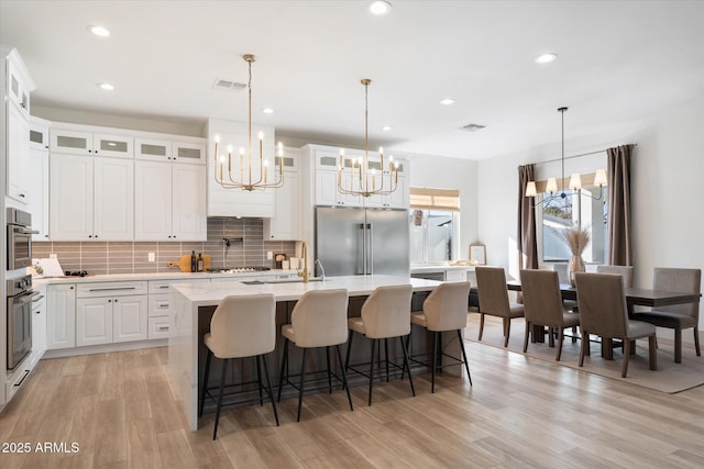 kitchen with decorative light fixtures, high end refrigerator, a kitchen island with sink, and white cabinets