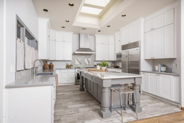 kitchen featuring wall chimney range hood, white cabinets, built in appliances, and a sink