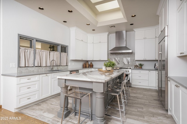 kitchen with a sink, high end stove, a kitchen bar, wall chimney exhaust hood, and tasteful backsplash