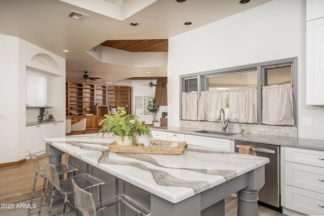 kitchen with white cabinets, stainless steel dishwasher, a kitchen bar, and a sink