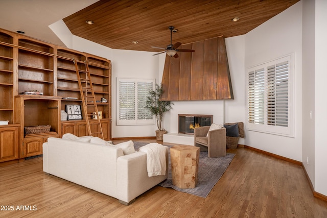 living area featuring wood finished floors, a glass covered fireplace, baseboards, wood ceiling, and ceiling fan