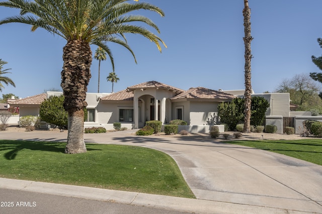 mediterranean / spanish home featuring fence, stucco siding, concrete driveway, a front lawn, and a tiled roof