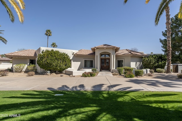 mediterranean / spanish-style house featuring a tiled roof, french doors, a front yard, and stucco siding