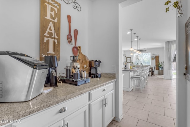 bar featuring white cabinets, hanging light fixtures, light tile floors, and light stone counters