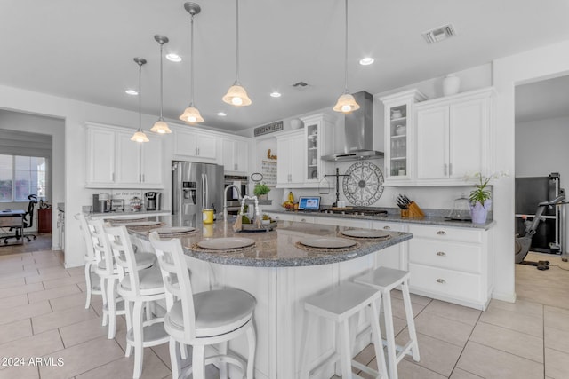 kitchen with appliances with stainless steel finishes, white cabinets, wall chimney exhaust hood, and decorative light fixtures