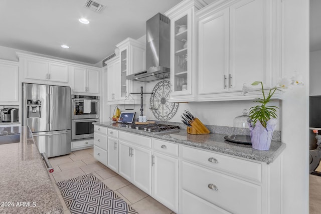 kitchen featuring stainless steel appliances, light tile flooring, wall chimney range hood, light stone counters, and white cabinets