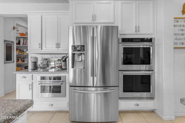 kitchen featuring white cabinets, light stone counters, appliances with stainless steel finishes, and light tile floors