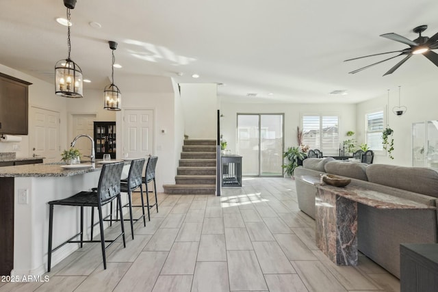 kitchen featuring dark brown cabinets, open floor plan, a breakfast bar, light stone counters, and a sink