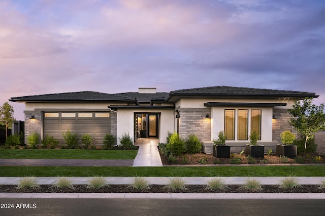 prairie-style home with a front lawn, an attached garage, stone siding, and stucco siding