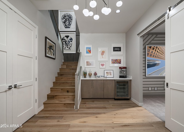 interior space with a barn door, wine cooler, a bar, light wood finished floors, and stairs