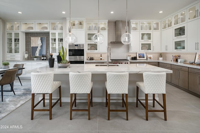 kitchen featuring wall chimney range hood, light tile patterned floors, decorative backsplash, stainless steel double oven, and a sink