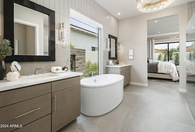 ensuite bathroom featuring ensuite bathroom, a sink, tile walls, a freestanding bath, and a chandelier