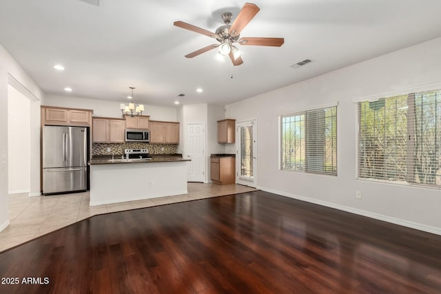 kitchen with light wood-style flooring, stainless steel appliances, dark countertops, ceiling fan with notable chandelier, and tasteful backsplash