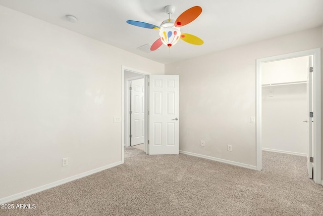 unfurnished bedroom featuring a ceiling fan, baseboards, carpet floors, a closet, and a walk in closet