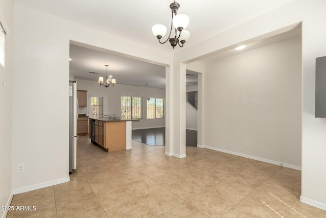 unfurnished living room with a chandelier, light tile patterned floors, baseboards, and a sink