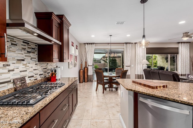 kitchen featuring pendant lighting, wall chimney exhaust hood, appliances with stainless steel finishes, tasteful backsplash, and light stone counters