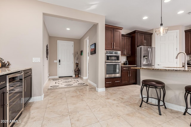 kitchen featuring light stone countertops, stainless steel appliances, pendant lighting, wine cooler, and a breakfast bar area