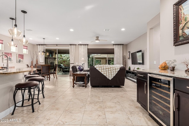 kitchen featuring light stone countertops, a breakfast bar, beverage cooler, ceiling fan, and hanging light fixtures