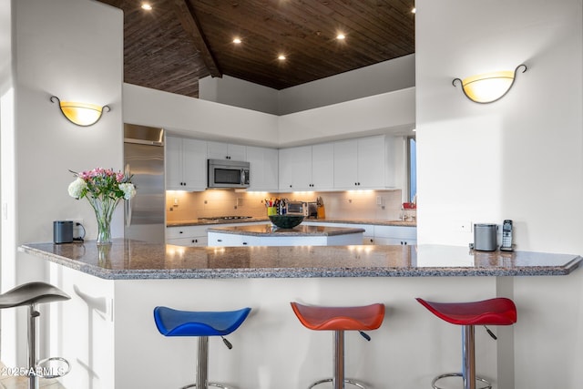 kitchen with wood ceiling, appliances with stainless steel finishes, backsplash, and stone countertops