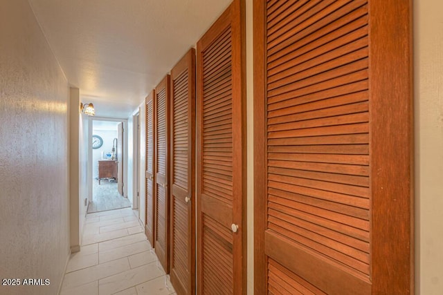 hall featuring light tile patterned floors and a textured wall