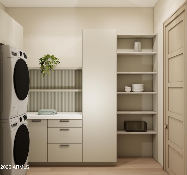 clothes washing area featuring stacked washer / drying machine, light hardwood / wood-style floors, and cabinets