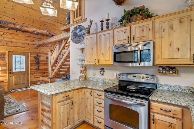 kitchen with kitchen peninsula, stainless steel appliances, light stone counters, and wood walls