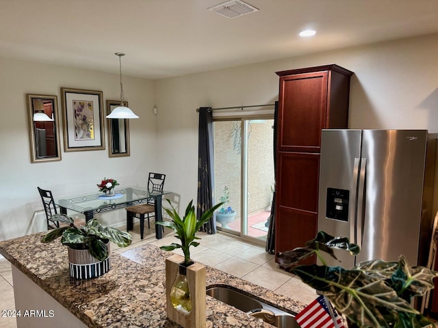 kitchen with dark stone counters, light tile patterned floors, pendant lighting, and stainless steel fridge with ice dispenser