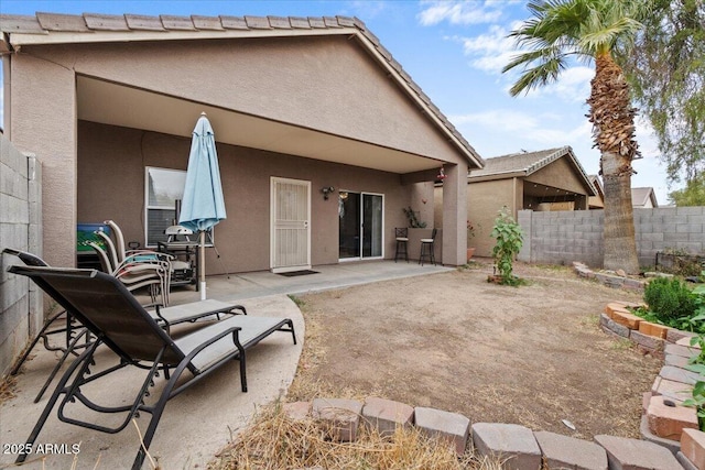 rear view of house with stucco siding, fence, a tile roof, and a patio area