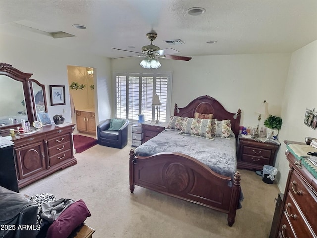 bedroom with light colored carpet, visible vents, a ceiling fan, connected bathroom, and a textured ceiling