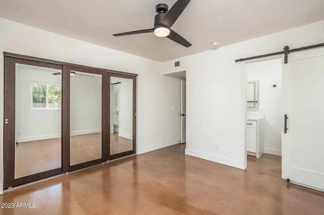 unfurnished bedroom featuring ensuite bath, concrete floors, a closet, ceiling fan, and a barn door