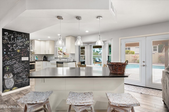 kitchen featuring white cabinets, french doors, stainless steel dishwasher, and hanging light fixtures