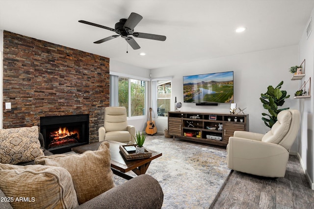 living room featuring hardwood / wood-style floors, ceiling fan, and a stone fireplace