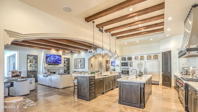 kitchen featuring dark brown cabinetry, a center island with sink, a kitchen bar, beam ceiling, and hanging light fixtures