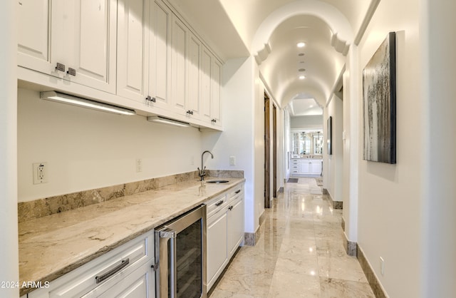 bar with light stone countertops, white cabinetry, wine cooler, and sink