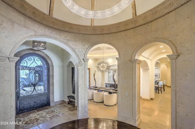 entryway featuring a towering ceiling, a chandelier, and decorative columns