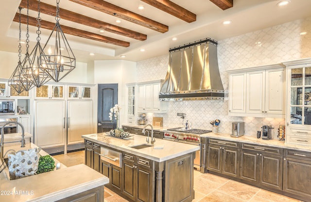 kitchen featuring wall chimney exhaust hood, beam ceiling, backsplash, an island with sink, and high end stainless steel range oven