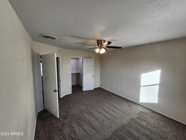 unfurnished bedroom with dark colored carpet, a textured ceiling, a closet, and ceiling fan